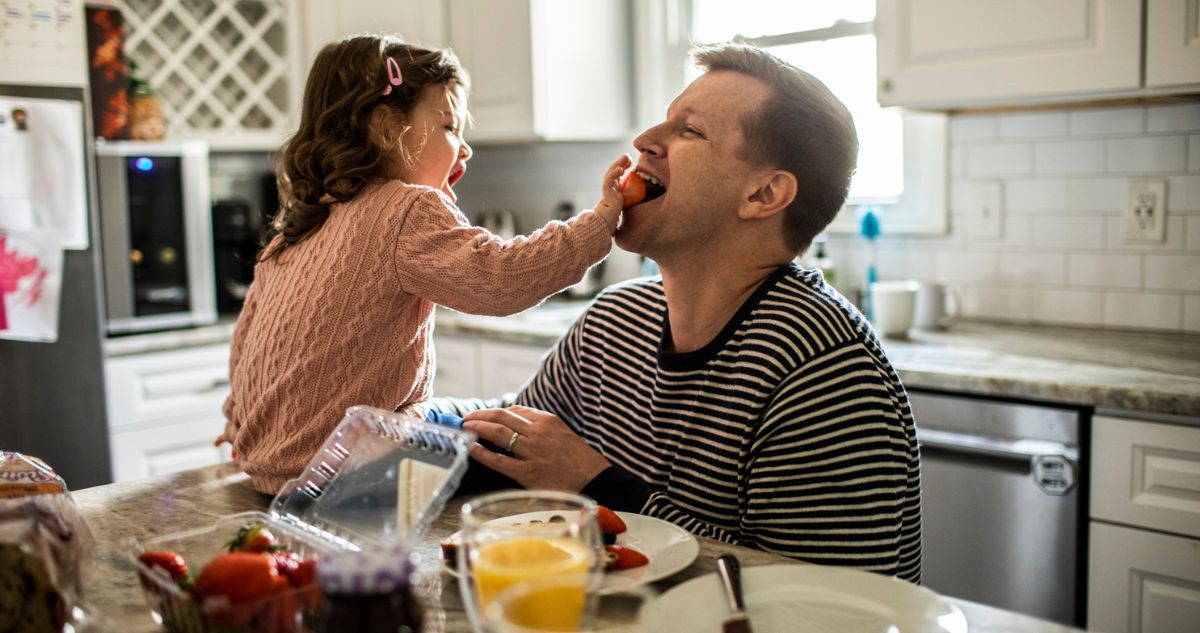kislány a konyhában az asztalon ülve apukáját eteti