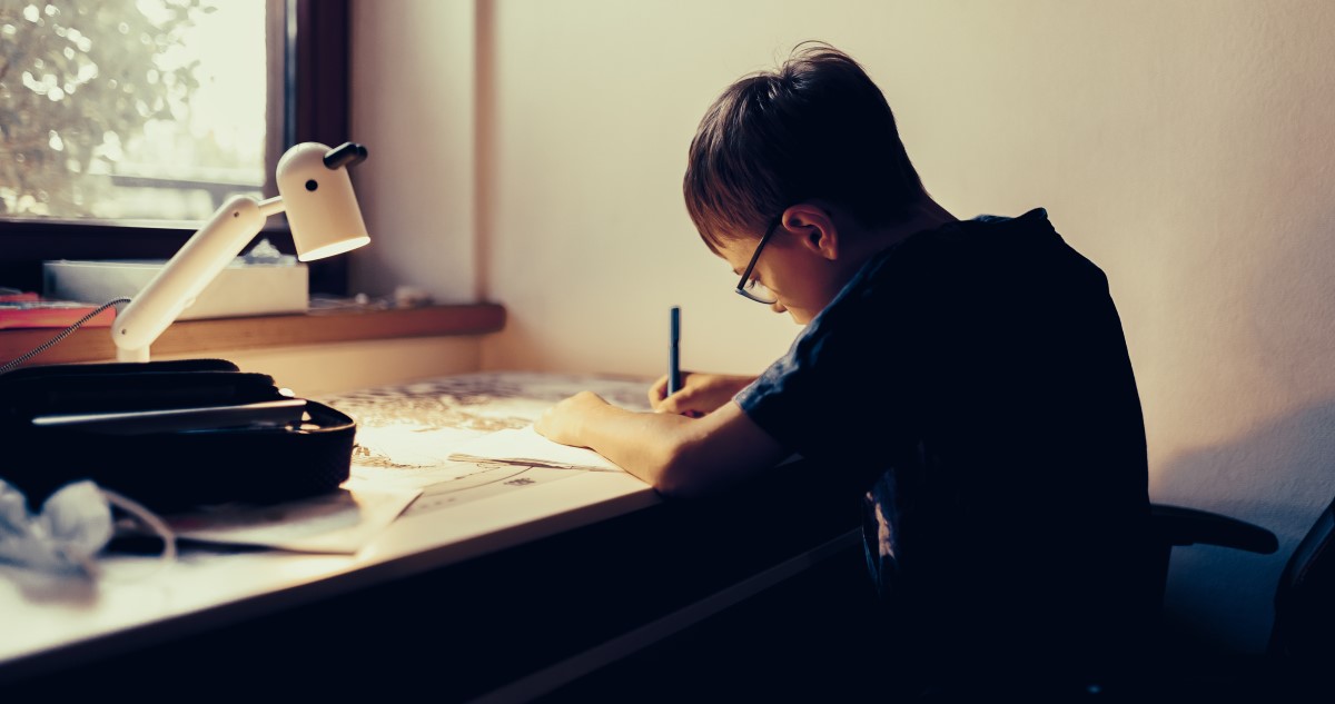 iskolás fiú leckét ír otthon az íróasztalnál