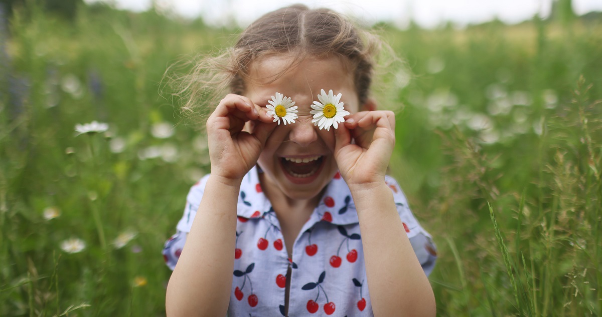 Kislány két virágot tart a szeme előtt a réten