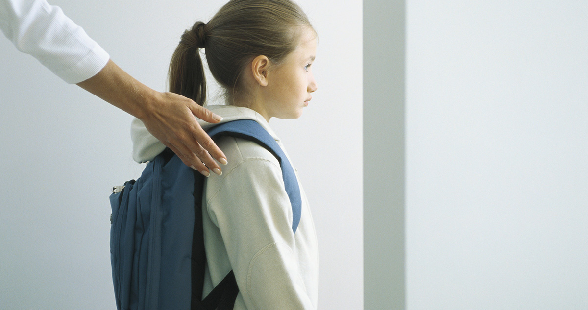 iskolás lány hátán táskával, az anya a vállára teszi a kezét