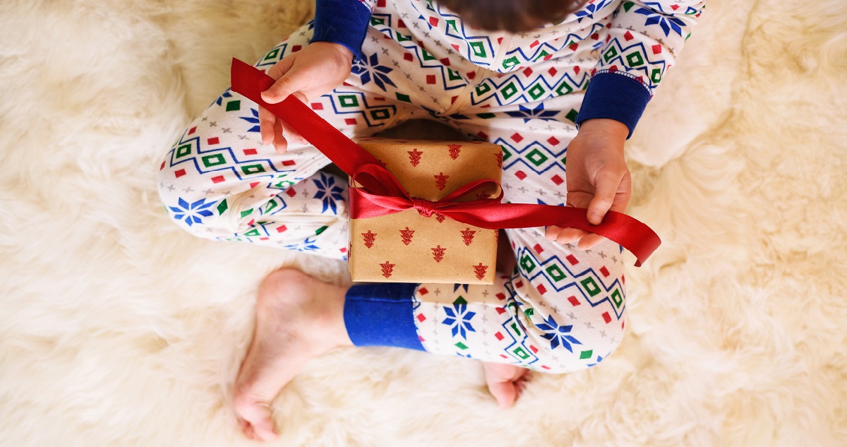Gyerek karácsonyi pizsiben ajándékot bont
