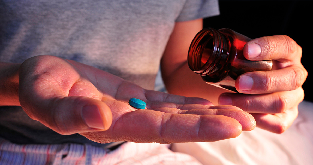 Férfi kezében kis kék tablettával