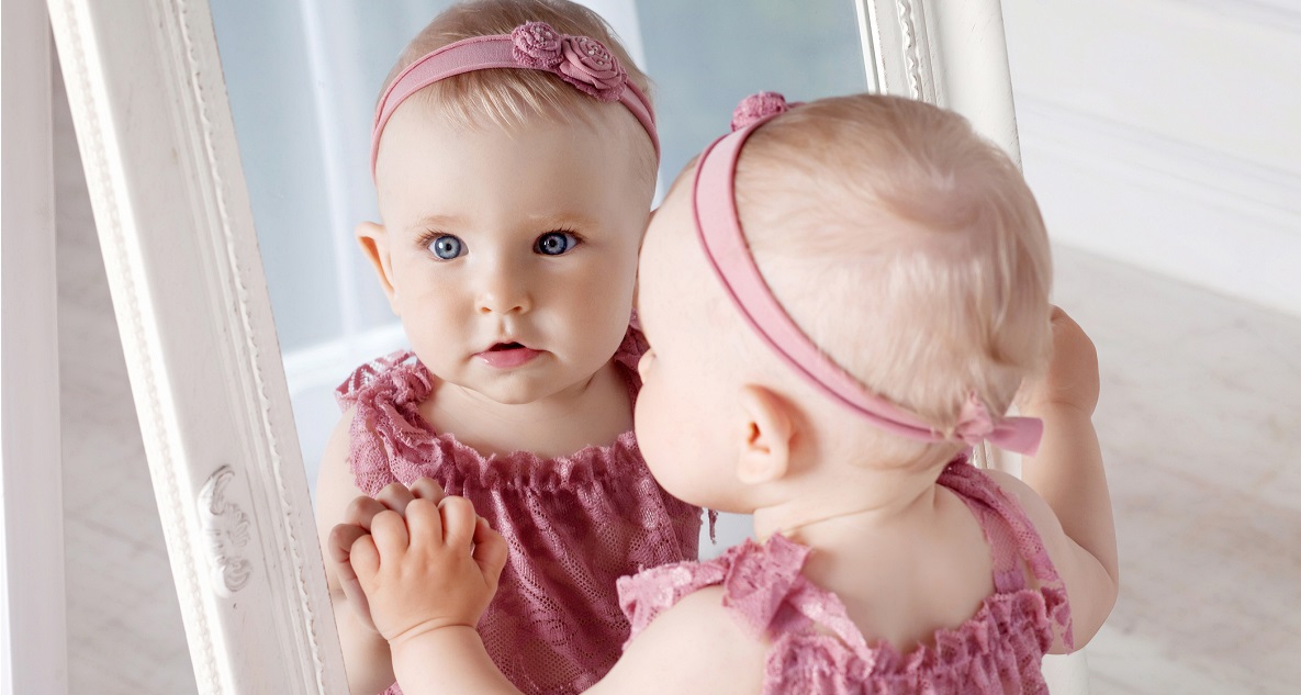 Kislány rózsaszín ruhában áll a tükör előtt