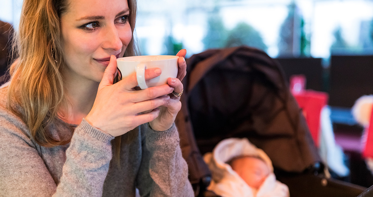 Kávét iszik háttérben baba babakocsiban