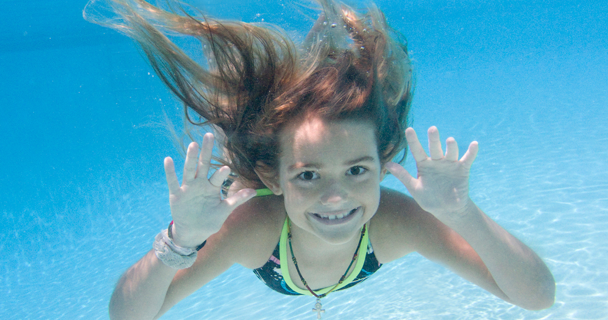 hosszú hajú, mosolygós kislány víz alatt úszik