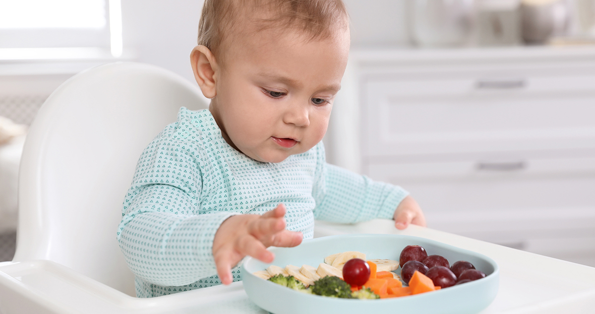 kisbaba etetőszékben szőlőt és zöldségeket eszik