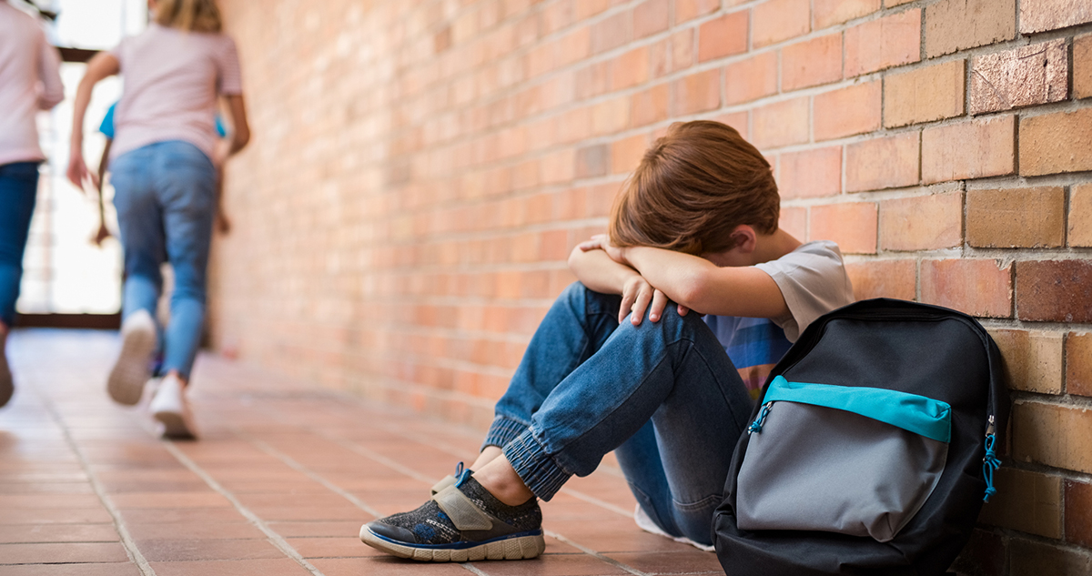 szomorú iskolás fiú ül a folyosón, zaklatás áldozata