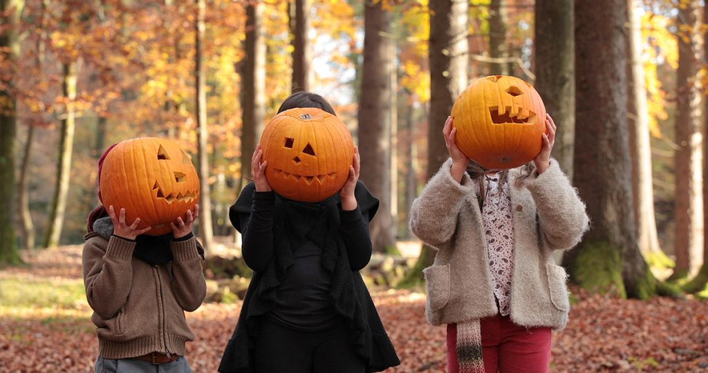 A halloweeni tökfaragás vicces családi program, és nem is bonyolult - Gyerekszoba Tökfaragás, gyerekek állnak az őszi erdőben halloween töklámpással az arcuk előtt