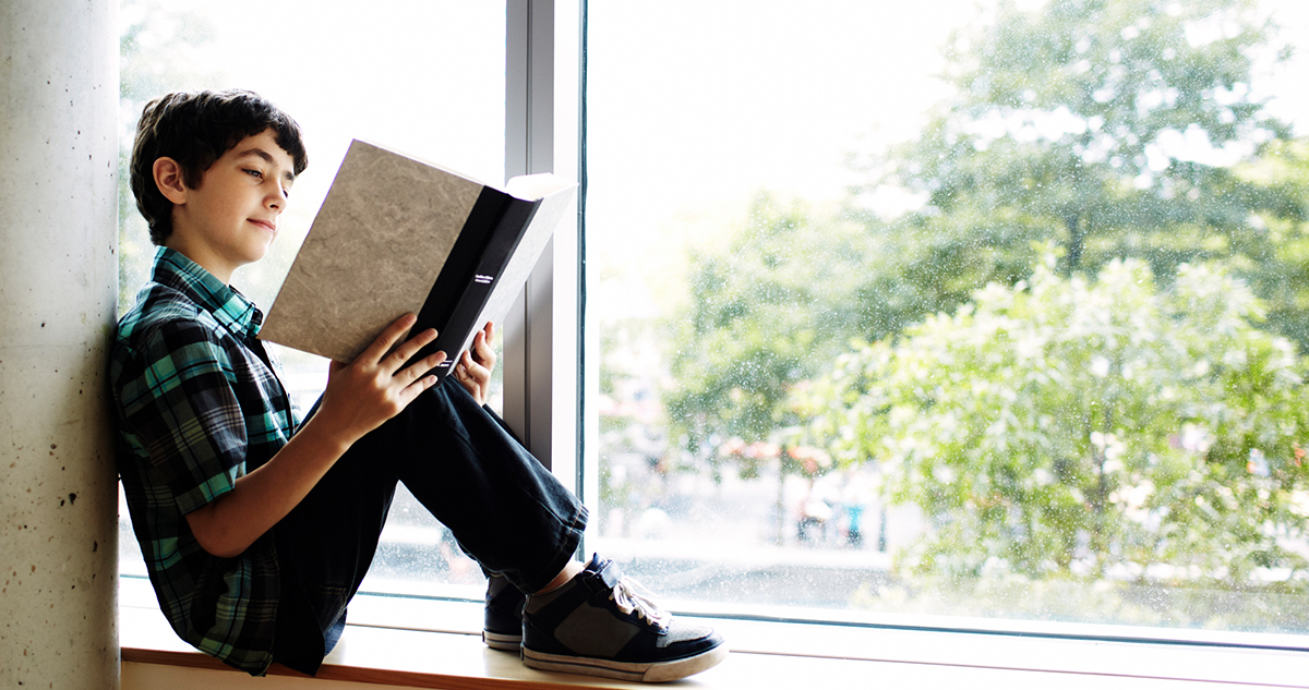 kisfiú olvas az ablakpárkányon ülve, vigyen könyvet az iskolába