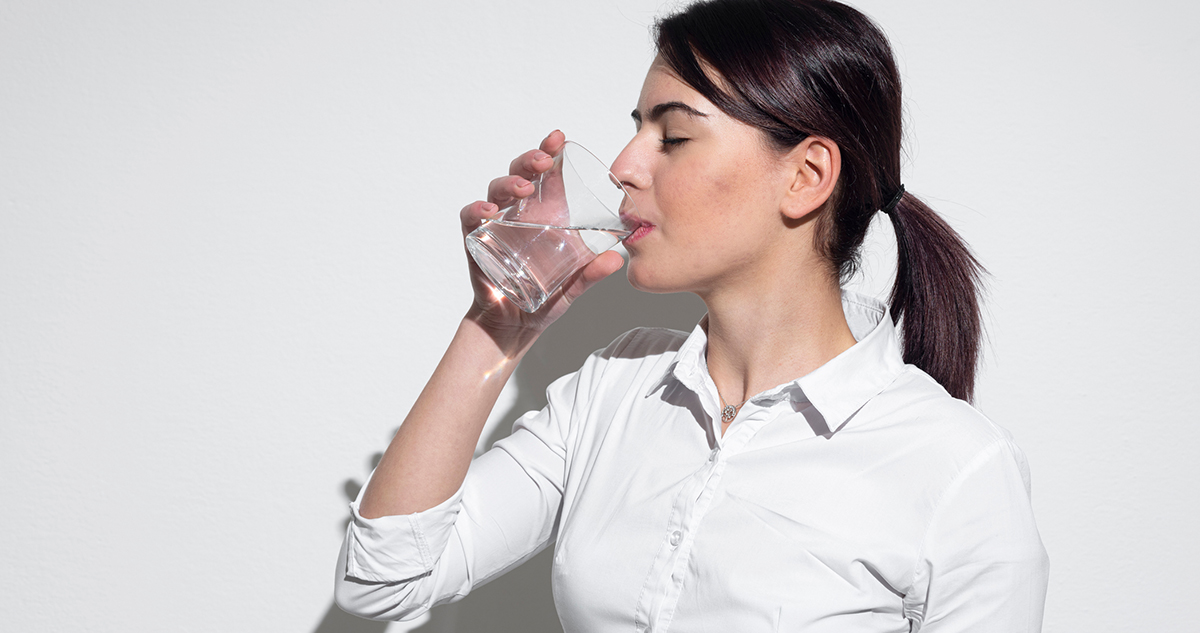 vidám nő vizet iszik, folyadékfogyasztás jótékony hatásai