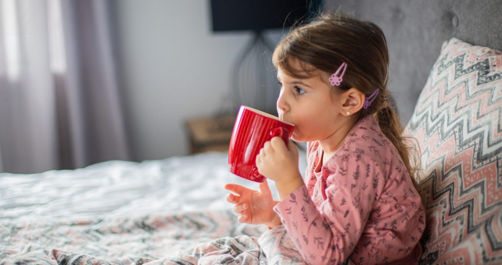 kislány ágyban fekve gyógyteát iszik, lándzsás útifű tea köhögésre