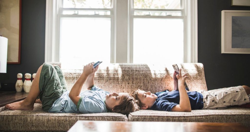 gyerekek a kanapén fekszenek a telefonjaikat nézik