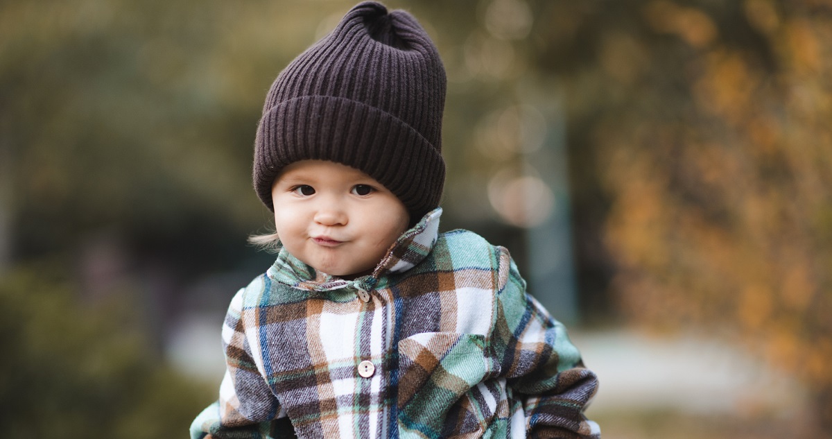 Funny baby girl 2-3 year old wearing knitted hat and checkered shirt walking in park outdoor. Autumn season.