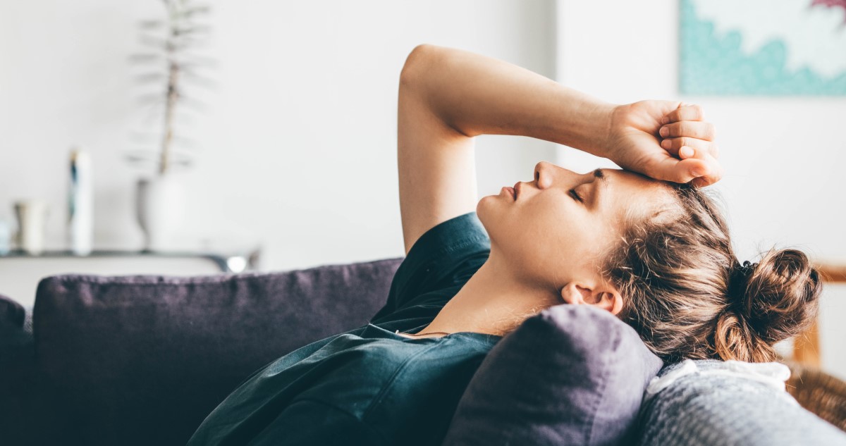 fáradt nő a kanapén ül a nappaliban és fogja a fejét