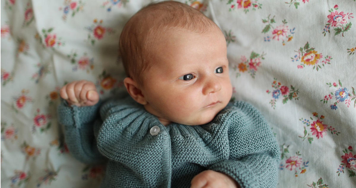Újszülött kislány szürke pulcsiban virágos takarón fekszik