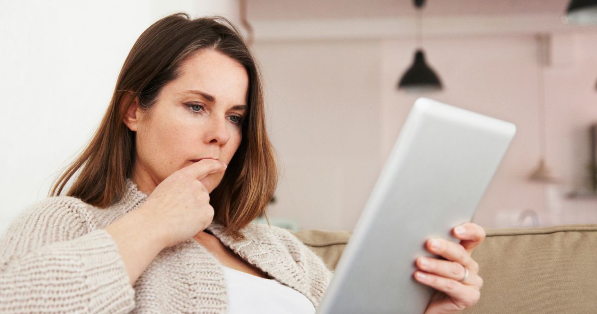 Középkorú nő a kanapén ülve gondolkodik a tabletjét bámulva