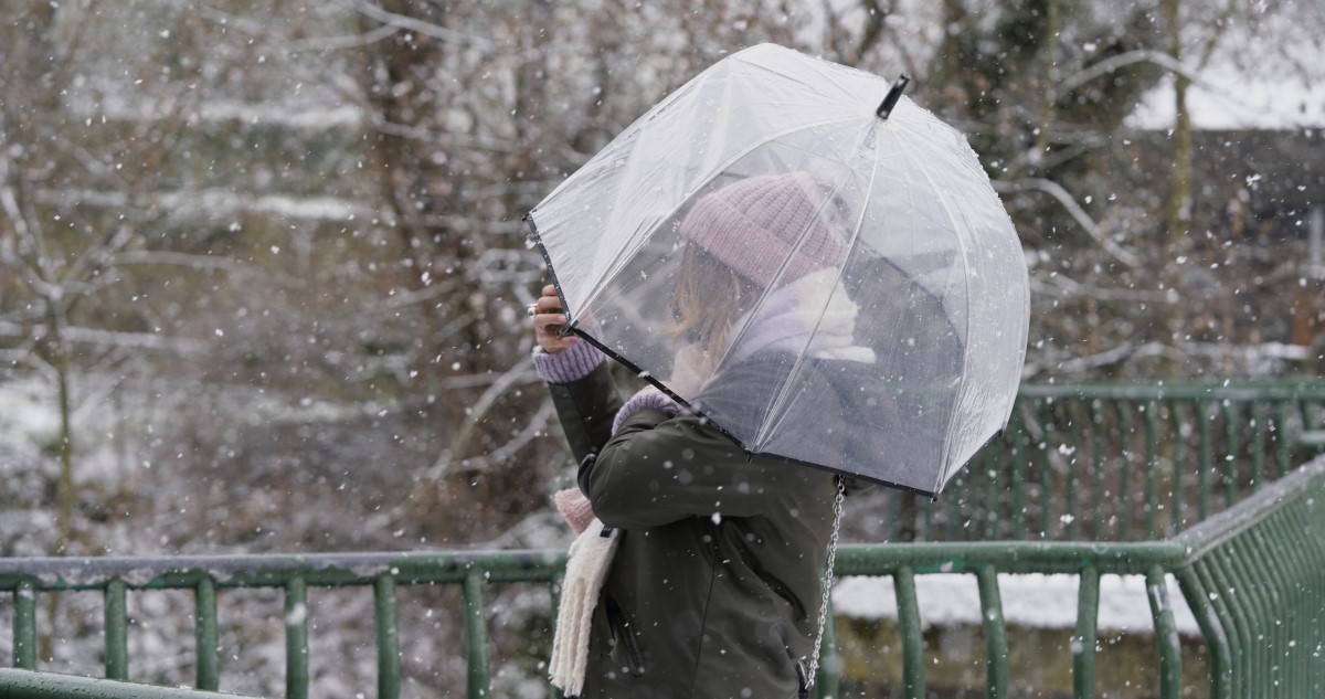 nő átlátszó esernyővel sétál át egy hídon havas esőben
