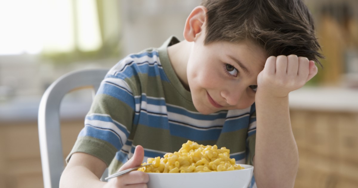 sajtos tésztát eszik egy kisfiú az asztalnál a konyhában