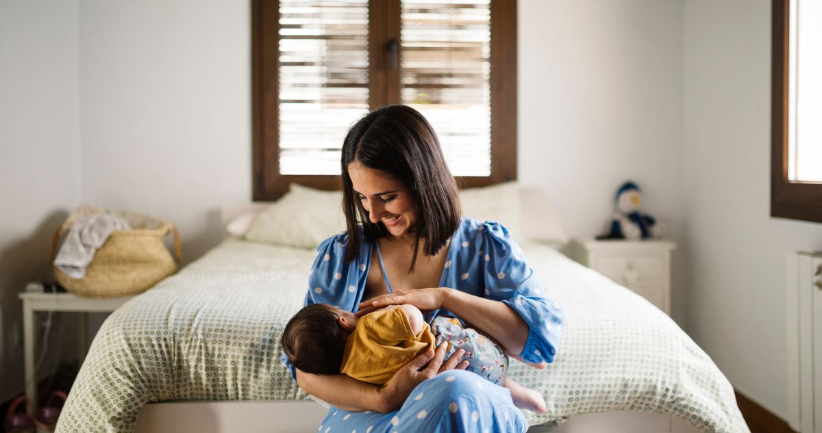 szoptatas - Gyerekszoba Anya mosolyogva szoptatja kisbabáját a hálószobában.