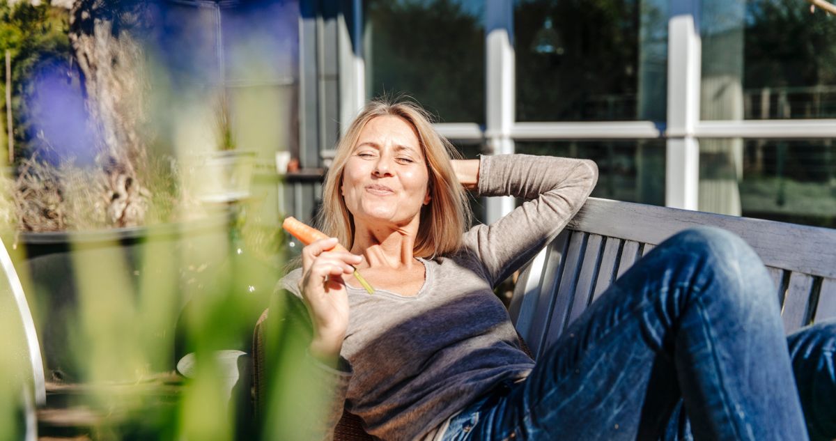 szőke nő mosolyogva sütkérezik a tavaszi napfényben a kertben