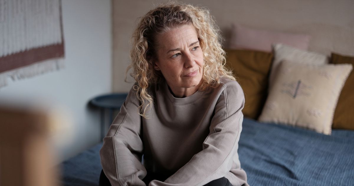 szőke középkorú nő tűnődve ül az ágyon
