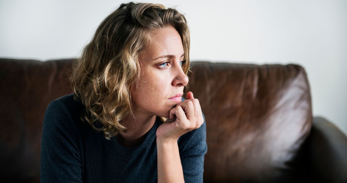 boldogtalan nő ül a bőr kanapén oldalra fordulva mered a semmibe