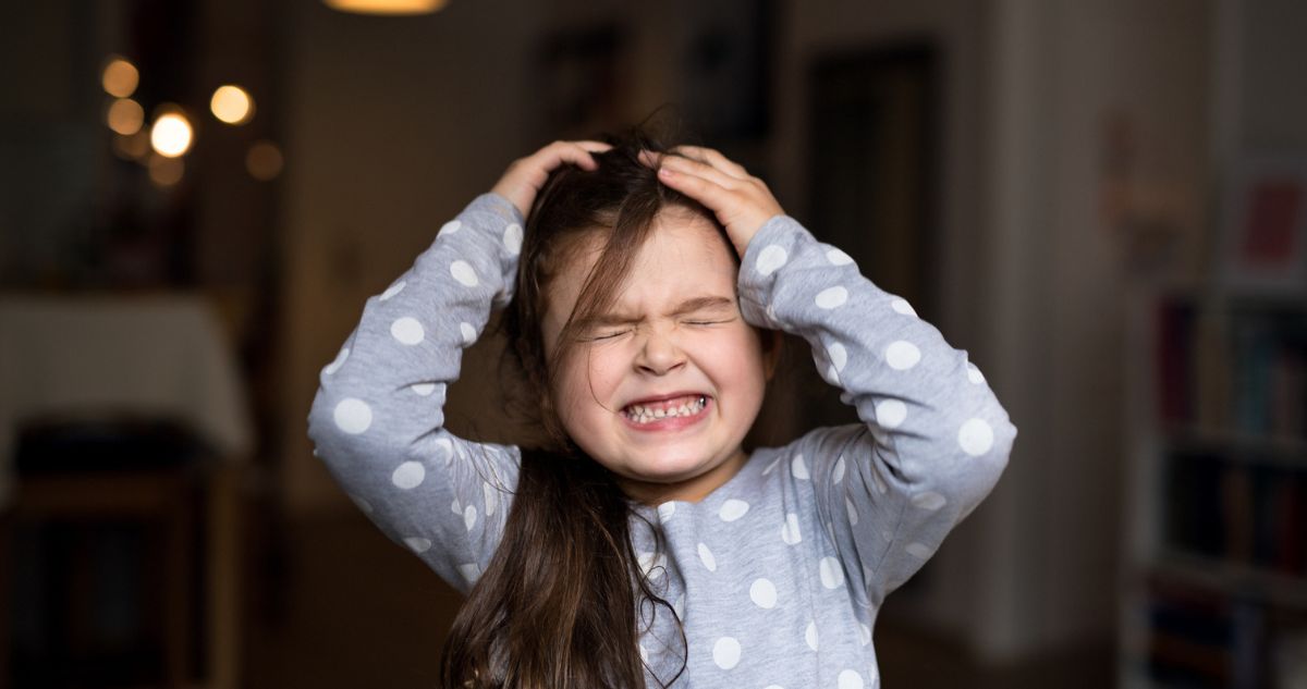 hisztis kislány a fejét fogja, vicsorít