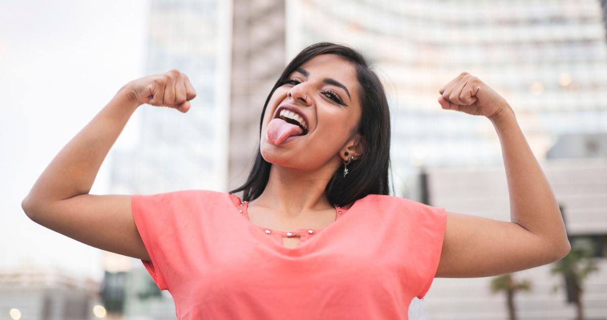 nő karját felemelve, nyelvét kinyújtva bicepszét mutatja