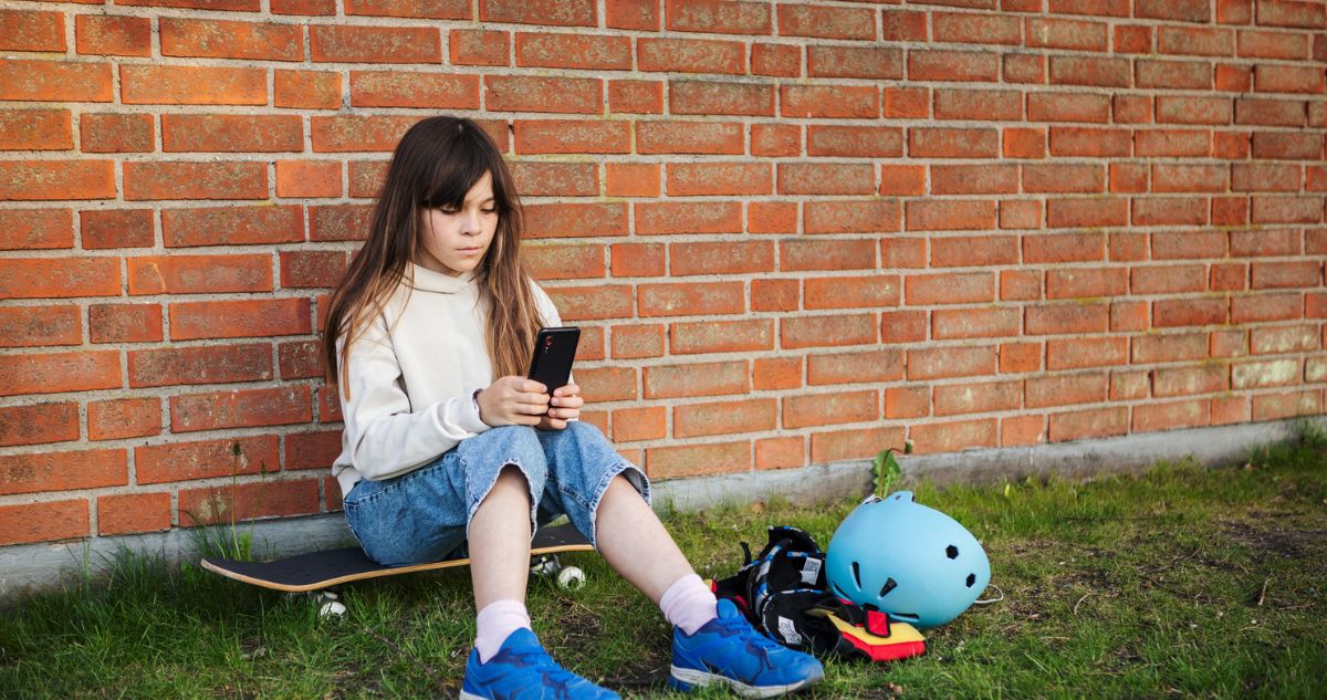 lány kezében telefonnal ül a gördeszkán