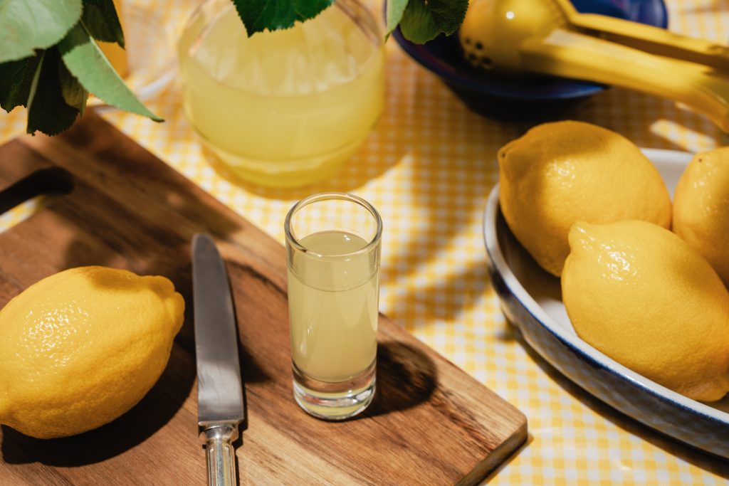 Garden table with limoncello shot glass and several fresh lemons on yellow table cloth Summer garden Elevated view - Gyerekszoba citromlé citrusok