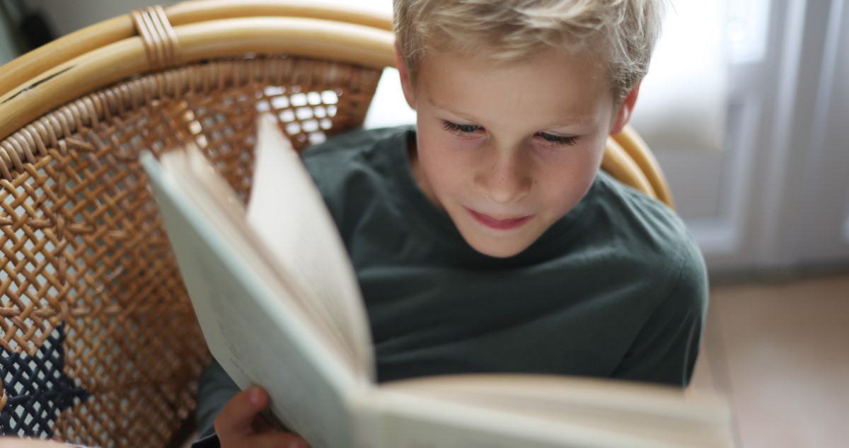 kisfiú olvas egy fotelban ülve
