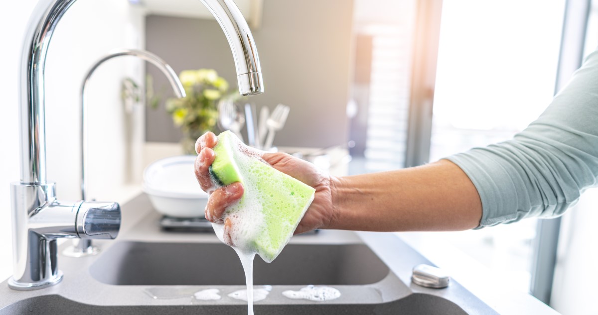 nő zöld mosogatószivacsot csavar ki a mosogató felett