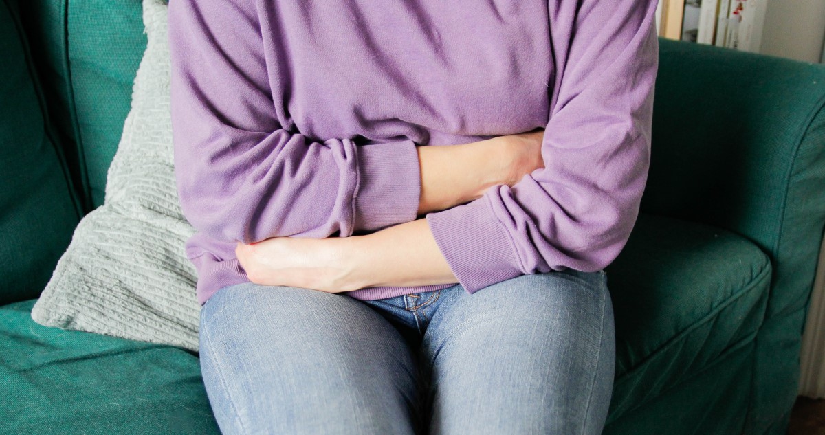 nő lila pulóverben fogja a hasát