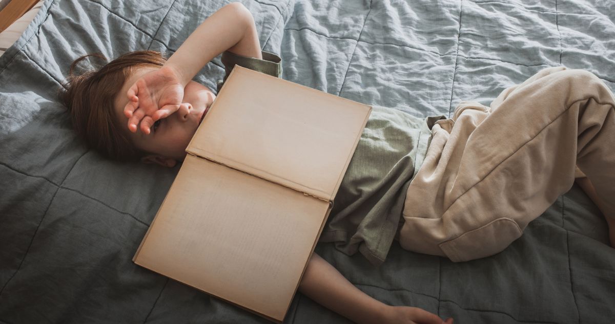 gyerek hanyatt fekszik az ágyon mellkasán könyvvel