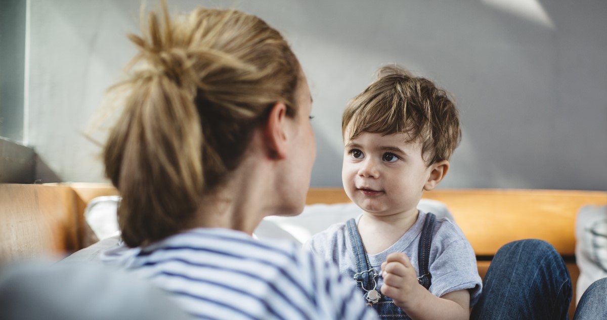 kék-fehér csíkos felsőben lévő édesanya beszélget hároméves kisfiával, aki az ölében ül