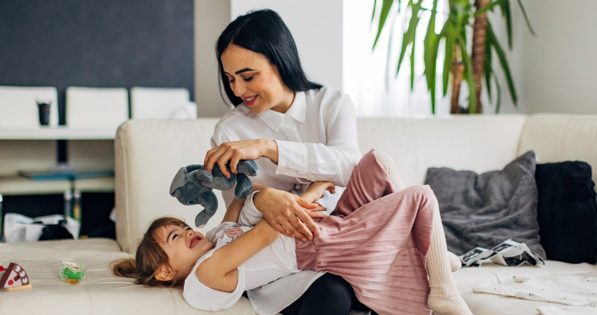 anya és kislánya a kanapén játszanak egy plüsselefánttal