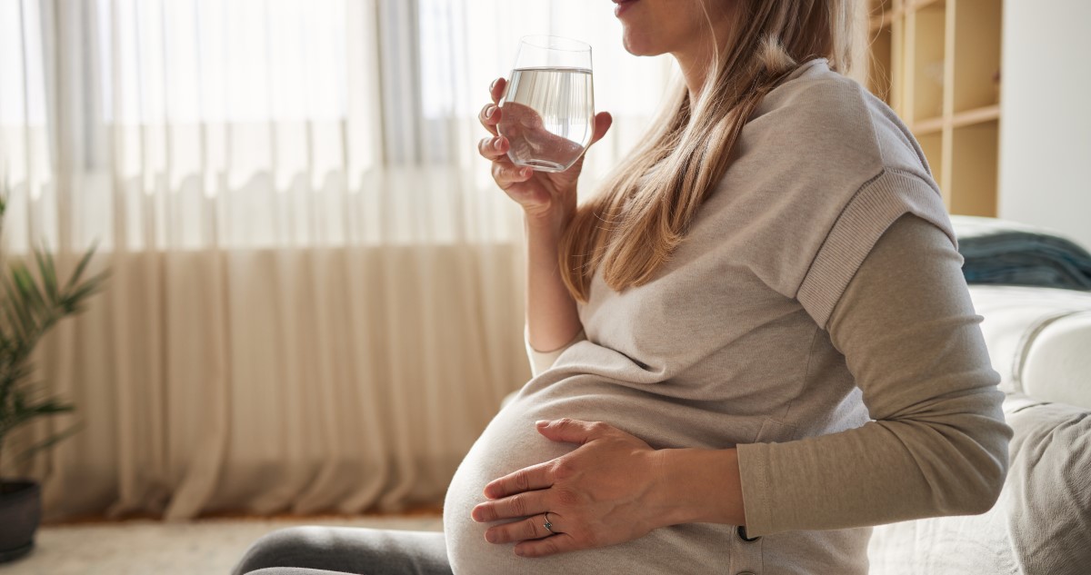 kismama pohárból iszik vizet, közben a pocakját fogja