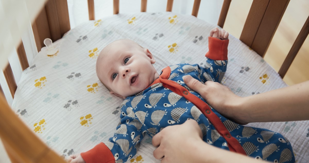 baba-ebren-van - Gyerekszoba A képen egy kisbaba látható, ki éppen felébredt a kiságyban, anyukája nyúl felé.