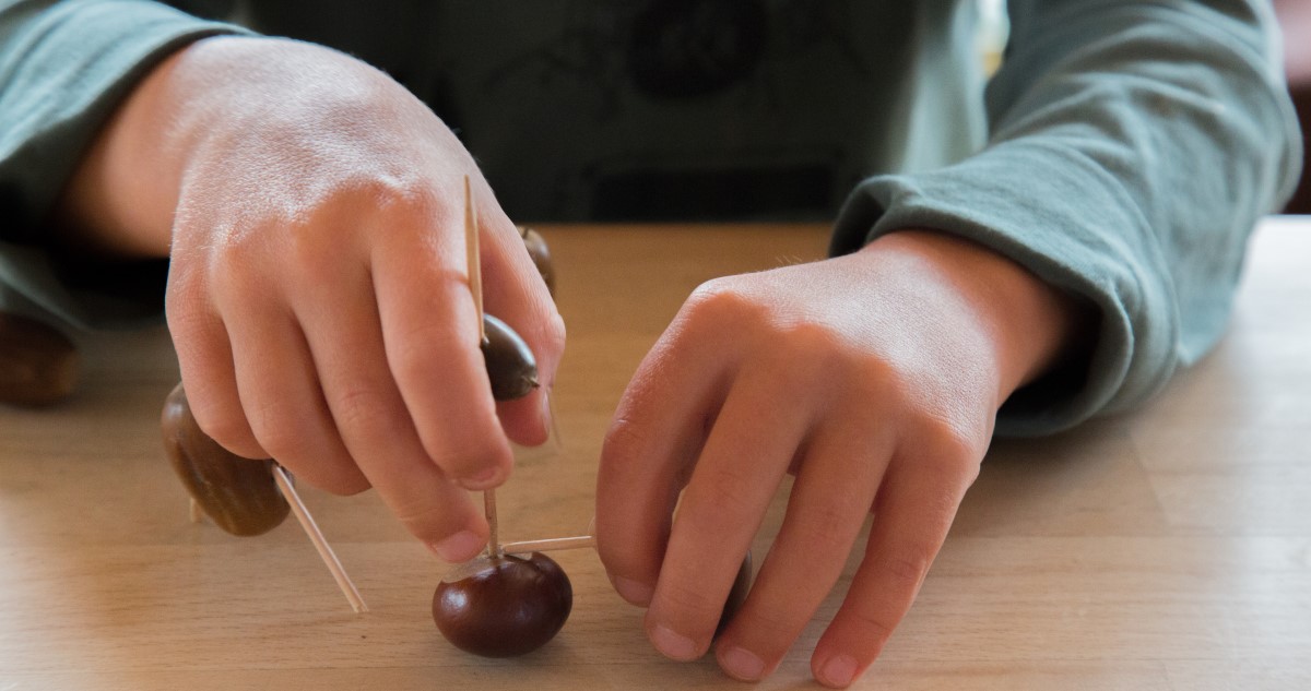 gesztenyefigurzas - Gyerekszoba A képen közelről látszanak egy kisfiú kezei, aki gesztenyéből alkot figurákat.
