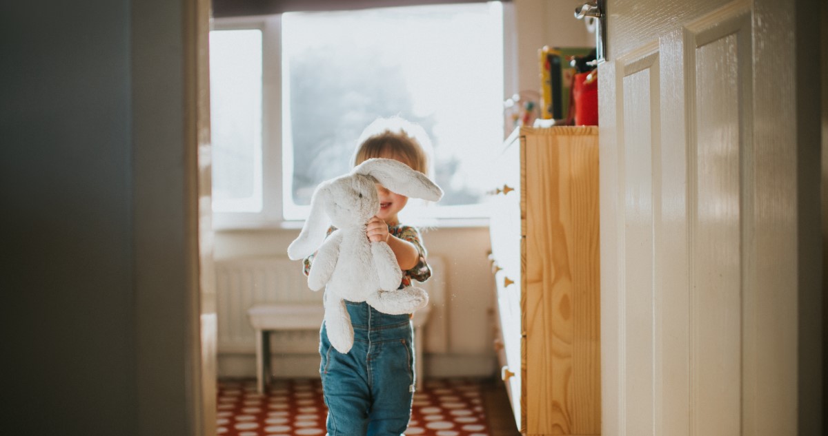 A képen egy kislány látható, aki egy plüssnyuszit tart a kezében a szobájában.